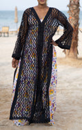 Long sheer black cover-up with a zigzag pattern with full-length sleeves and a bold chevron pattern. Features a lightweight, flowy design with a black button-down front closure, perfect for layering over swimwear or resort outfits. Styled over a floral dress on a beach.