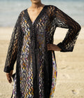Long sheer black cover-up with a zigzag pattern with full-length sleeves and a bold chevron pattern. Features a lightweight, flowy design with a black button-down front closure, perfect for layering over swimwear or resort outfits. Styled over a floral dress on a beach.