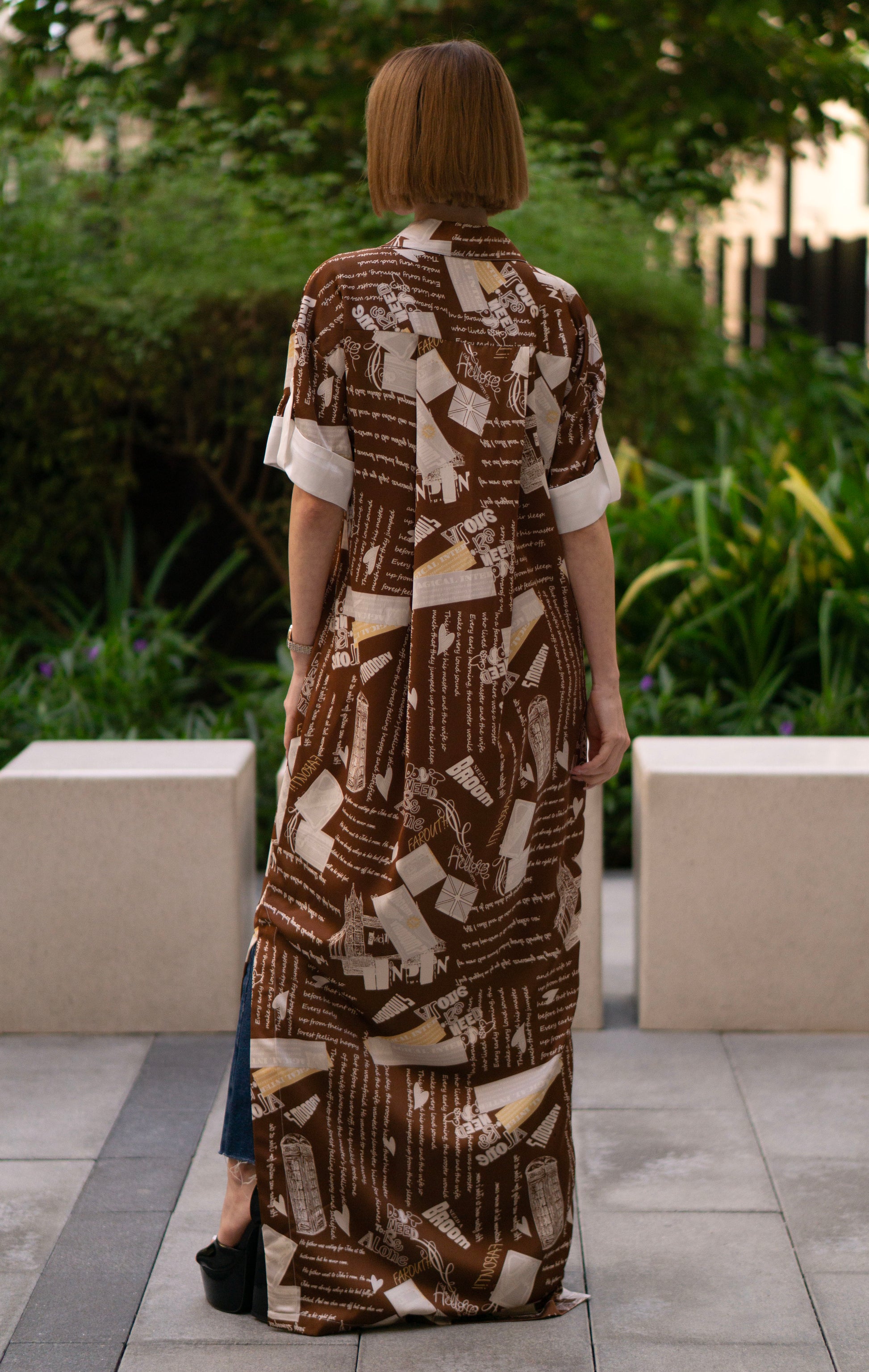 Back view of the printed brown shirt dress with side slits, women’s full-length button-down shirt dress featuring artistic script print and short sleeves