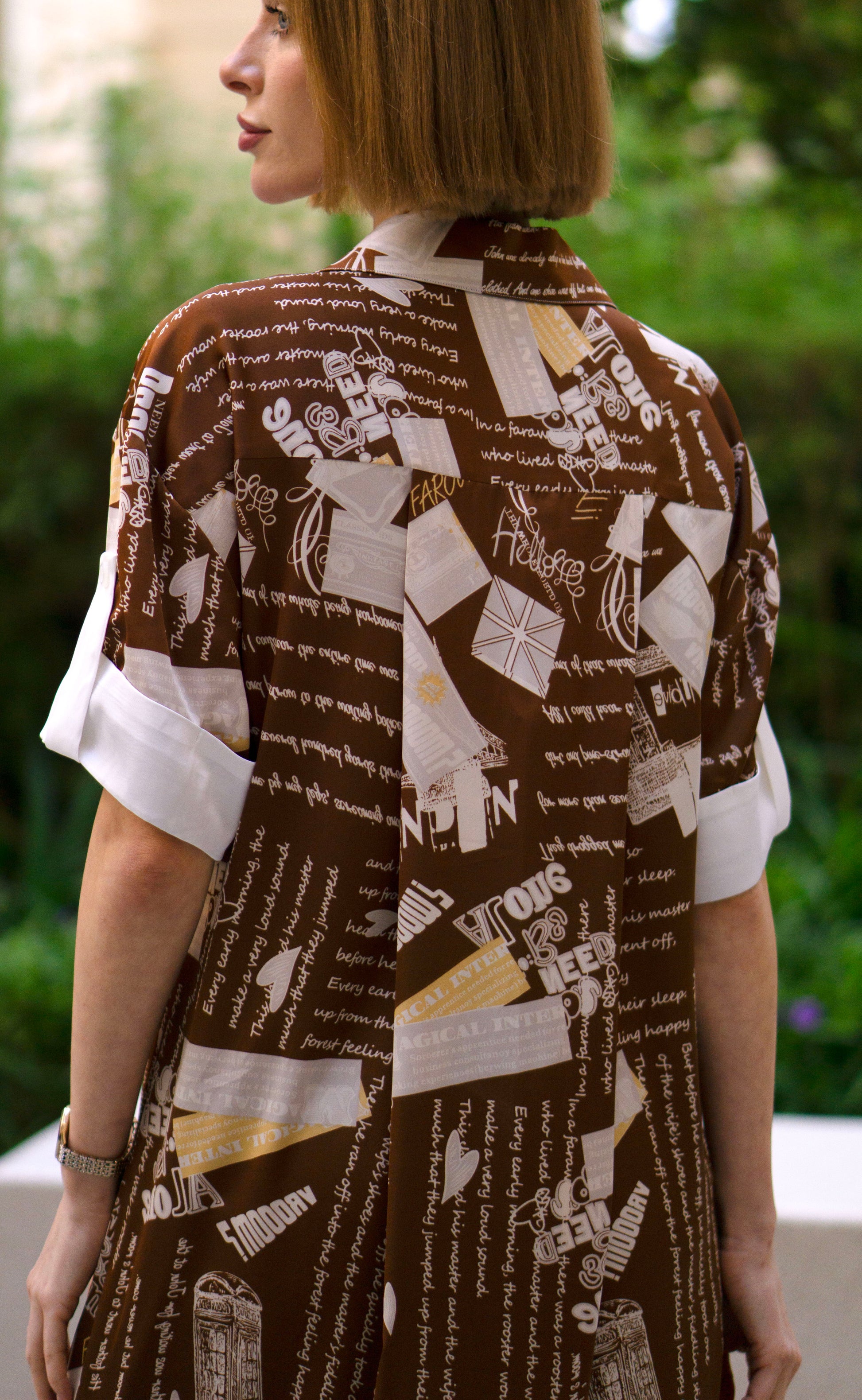 Back view of printed brown shirt dress with side slits, women’s full-length button-down shirt dress featuring artistic script print and short sleeves